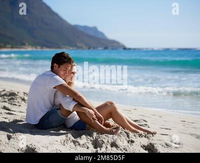 Condividere un momento tranquillo insieme. Una giovane coppia seduta insieme sulla spiaggia e ammirando la splendida vista. Foto Stock