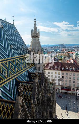 Dalla cima della Cattedrale di Santo Stefano a Vienna, un bellissimo tetto piastrellato, vedute della città e di alcuni operai che eseguono lavori di manutenzione sopra la città Foto Stock