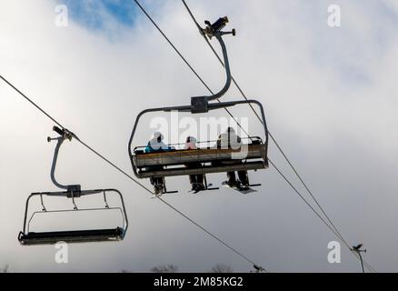 Vista posteriore di tre persone che cavalcano su uno skilift per lo snowboard e sciare giù per il Monte Snow n Vermont. Foto Stock