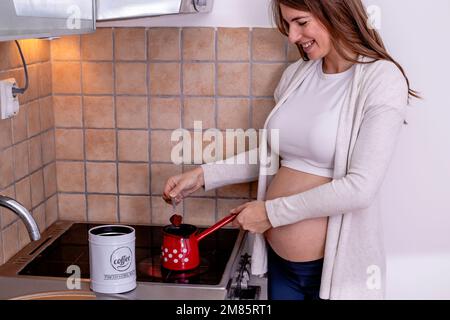Una giovane donna incinta che fa il caffè in cucina. Foto Stock