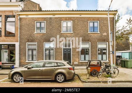 una macchina parcheggiata di fronte ad una casa con due biciclette sulla strada accanto ad essa e una bici appoggiata al muro Foto Stock