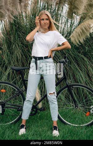 Giovane bella ragazza sta posando in una t-shirt bianca accanto alla sua moto. Mockup verticale. Foto Stock