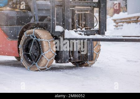 Ruota del trattore con catena. Trattore o caricatore su una strada sdrucciolevole e innevata. I caricatori si azionano sulla neve con catene antislittamento. Foto Stock