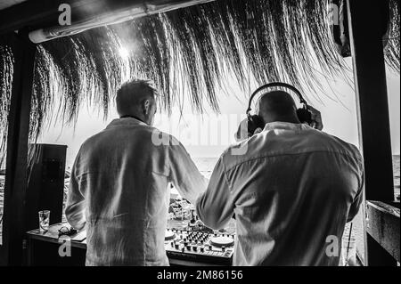 Vista posteriore dei jockeys del disco che suonano musica per i turisti al club party all'aperto sulla spiaggia - DJ che indossano le cuffie all'evento musicale dal vivo - Musica An Foto Stock