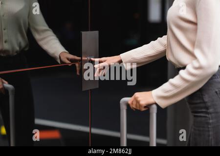 vista parziale della donna in piedi vicino a porte riflettenti dell'ascensore e premendo il pulsante di chiamata, immagine stock Foto Stock