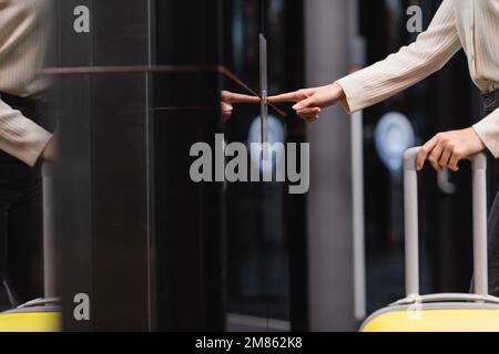 vista ritagliata della donna con borsa da viaggio premendo il pulsante di chiamata ascensore in hotel, immagine stock Foto Stock