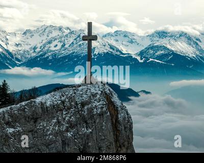 Prospettiva droni della croce di legno Croix du Nivolet ai margini della Dent du Nivolet, nel massiccio di Bauges, con la catena montuosa delle alpi innevate alle spalle Foto Stock
