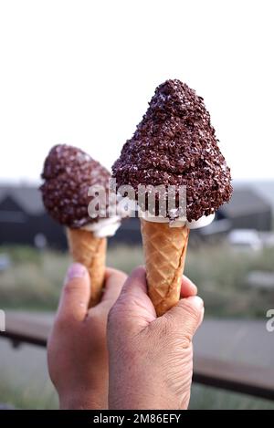 Un colpo verticale di mani che tengono coni di gelato ricoperti di gocce di cioccolato Foto Stock