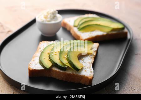 Piatto di gustosi panini con formaggio cremoso e avocado su sfondo colorato, primo piano Foto Stock