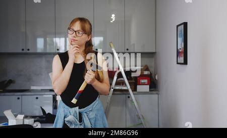 donna con gli occhiali che indossano una camicia nera senza maniche e che tiene un martello, pensando alla riparazione. Foto di alta qualità Foto Stock