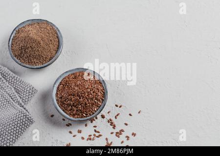 Semi di lino marroni e semi di lino macinati o frantumati in una piccola ciotola su fondo grigio chiaro. Foto Stock