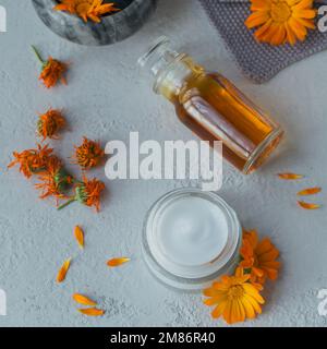 Una bottiglia di tintura di marigold della pentola o infusione, unguento, crema o balsamo con i fiori freschi e asciutti di Calendula su fondo chiaro. Erbe naturali Foto Stock