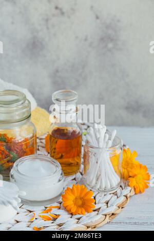 Una bottiglia di tintura di marigold o infusione, unguento, crema o balsamo con fiori di calendula freschi e secchi e tampone di cotone e si stende su un bianco Foto Stock