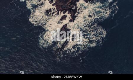 Le acque scure e imponenti dell'oceano si schiantano ferocemente contro una scogliera aspro. Foto Stock