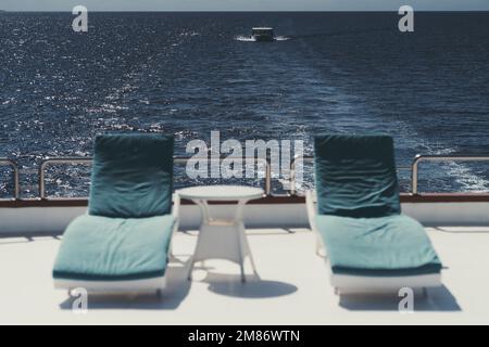 Inquadratura grandangolare di una barca con messa a fuoco selettiva sullo sfondo mentre in primo piano due poltrone reclinabili con cuscini blu e un tavolino da caffè, al Foto Stock