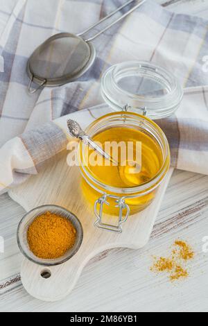 Sano ghee fatto in casa o burro chiarificato in un vaso e curcuma in polvere su tavolo di legno bianco. Concetto alimentare Ayurveda sano. Foto Stock