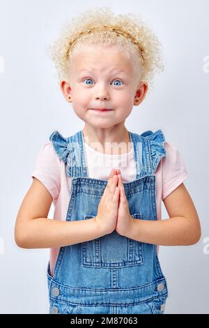 ritratto di una bambina sorridente e carina dai capelli biondi. felice ragazzo bello tenere le mani insieme isolato su sfondo bianco, bambino guardando il camer Foto Stock