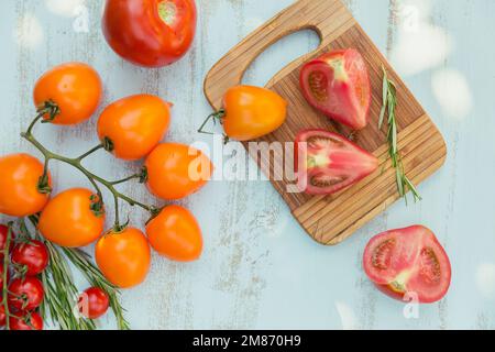 Vari pomodori colorati e erbe di rosmarino su sfondo azzurro Foto Stock