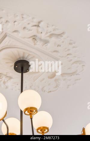 un chandel appeso al soffitto in una stanza con carta da parati bianca e rifiniture dorate intorno all'apparecchio di illuminazione Foto Stock