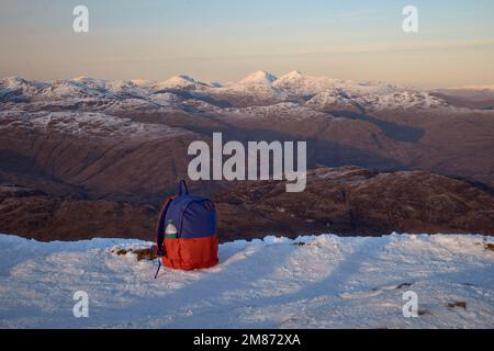 Vista serale dalla cima di ben Lomond alle vicine cime al tramonto. In primo piano uno zaino da trekking sulla neve. Loch Lomond e il Parco Nazionale Trossachs. Scozia Foto Stock