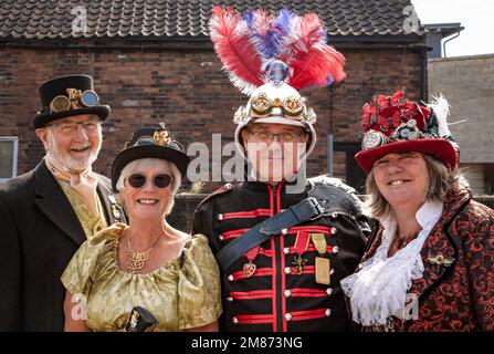 Ritratto di un gruppo di punk a vapore di mezza età che indossano abiti Steampunk militari e d'epoca. Sorridendo, ridendo e guardando direttamente nella fotocamera. Foto Stock