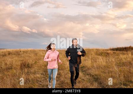 Giovane coppia che corre sul campo in mattinata. Uomo e donna caucasici in allenamento da jogging, in abbigliamento sportivo. Esercizio maschile e femminile, formazione insieme Foto Stock