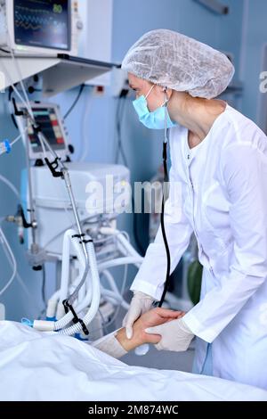 Medico caucasico esperto in Robe medico che verifica il polso del paziente sdraiato sul letto, tenendo la mano della persona malata. Nel moderno ospedale di Ward, Foto Stock