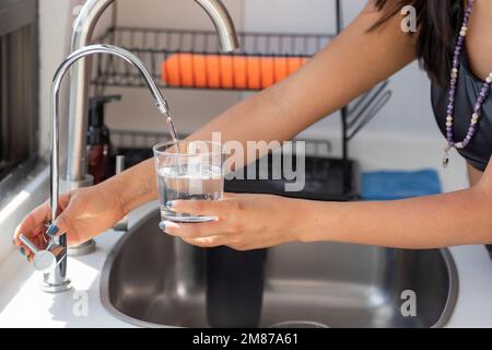 Le mani di una donna che tiene un bicchiere che si riempie di acqua dal filtro del rubinetto. Foto Stock