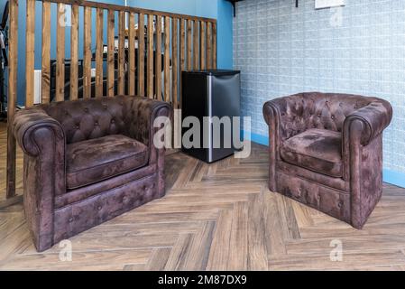 Angolo di un salone di bellezza con divani chester individuali con pelle girata e pareti blu Foto Stock