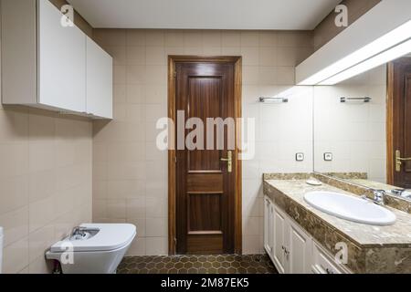 Bagno in tonalità bianche e crema con lavabo in legno con piano in marmo, lavello in porcellana bianca, specchio integrato e porta in legno di sapele Foto Stock