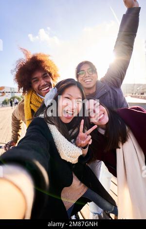 Allegro gruppo di amici che prendono un selfie all'aperto in città, sorridendo e guardando la macchina fotografica. Foto Stock