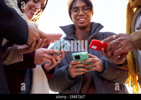 Quattro amici multirazziali che si riuniscono in cerchio utilizzando il telefono all'aperto. Foto Stock