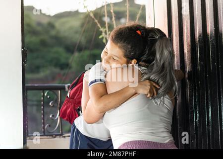 giovane madre che dice Arrivederci alla figlia prima di partire per la scuola. donna che dà un abbraccio alla bambina. Foto Stock