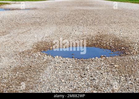 Buche, buca, in strada di ghiaia. Concetto di riparazione, manutenzione e danneggiamento di strade rocciose Foto Stock