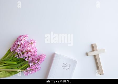 Bordo bianco della Bibbia del Santo Cristiano, piccola croce di legno e bouquet di fiori freschi rosa giacinto su sfondo bianco con spazio copia Foto Stock