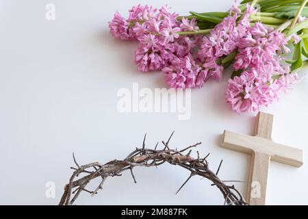 Semplice croce di legno e corona di spine con fiori rosa giacinto su sfondo bianco con spazio copia Foto Stock