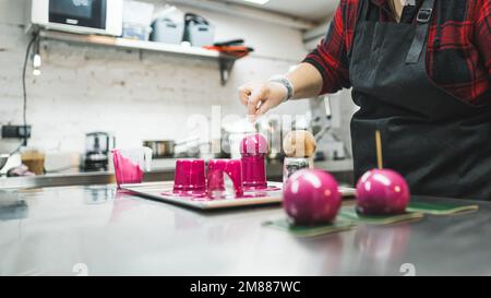 vista laterale di un panettiere che decorano palline di cioccolato con crema rosa nel panificio, concetto dessert. Foto di alta qualità Foto Stock