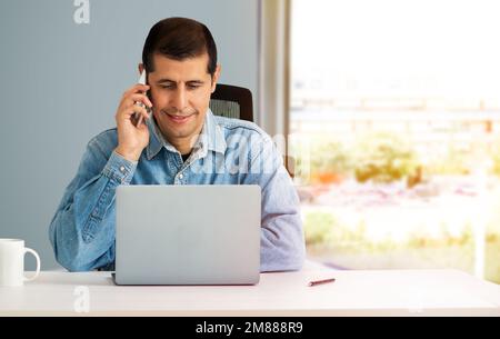 Foto di un giovane uomo d'affari che parla al telefono e usa un computer portatile al lavoro Foto Stock
