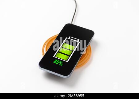 Primo piano della ricarica wireless del moderno smartphone nero touchscreen in metallo lucido sul caricabatterie wireless, con indicatore di ricarica al 85% in verde Foto Stock