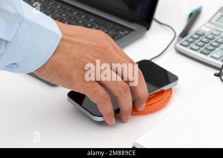Mano di un uomo d'affari che carica il suo smartphone con un caricabatterie wireless in ufficio Foto Stock