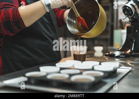 baker mettere l'impasto da una ciotola in una tazza di plastica per preparare muffin al cioccolato. Foto di alta qualità Foto Stock