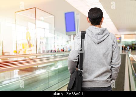 Ripresa da dietro di un giovane uomo irriconoscibile in piedi su una passerella in movimento nell'aeroporto Foto Stock