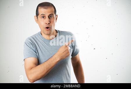 Bell'uomo che indossa casual camicia grigia su sfondo parete di cemento sorpreso puntando con il dito a lato, bocca aperta espressione stupita. Foto Stock