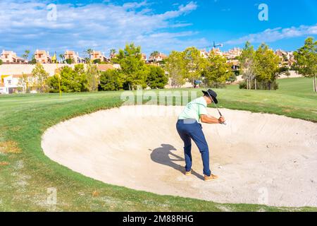 Uomo che gioca a golf, nel bunker che colpisce la palla con il bastone pitching cuneo Foto Stock