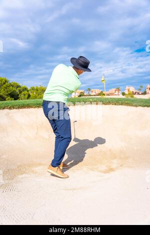 Uomo che gioca a golf, ottenendo la sfera dal bunker colpendo la sfera con il bastone del cuneo di beccheggio Foto Stock