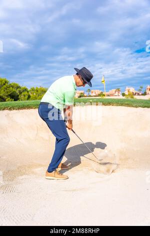 Uomo che gioca a golf, nel bunker che colpisce la palla con il bastone pitching cuneo Foto Stock