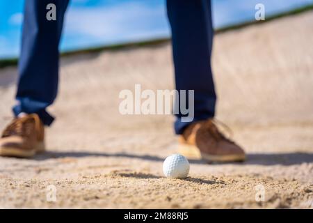 Piedi di un uomo che gioca a golf, nel bunker che colpisce la palla con il cuneo di lancio bastone Foto Stock