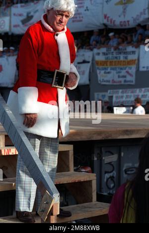 L'Entertainer Bob Hope si trova sui gradini del palcoscenico vestito con un cappotto e cappello rosso di Babbo Natale durante il suo spettacolo della United Services Organization (USO) a bordo della nave d'assalto anfibia USS OKINAWA (LPH-3). Base: Sitrah Paese: Bahrain (BHR) Foto Stock