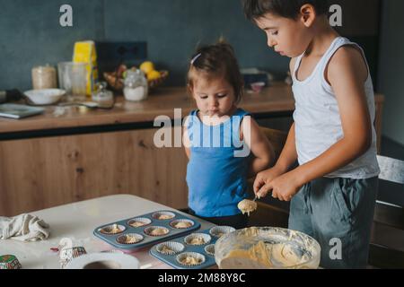 Bambini mettere l'impasto per cuocere i cupcake. Concetto di famiglia amichevole, assistenza reciproca, sostegno, cucina. Foto Stock