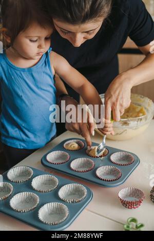 Madre e figlia versano pasta cruda in stampi di silicone. Festa della mamma, famiglia, cottura casalinga cibo sano Foto Stock